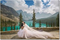 a bride and groom standing on the edge of a cliff overlooking a beautiful mountain lake