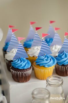 cupcakes with blue frosting and sailboats on them are sitting on a table