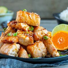 chicken with sauce and green onions on a black plate next to an orange, rice and lime wedges