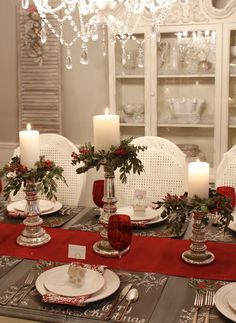 the table is set for christmas dinner with red and white place settings, silverware and candles