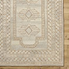 a beige rug with an intricate design on the top and bottom, sitting on a wooden floor