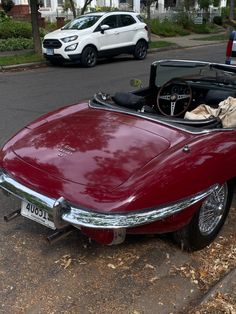 an old red sports car parked on the side of the road with its hood open