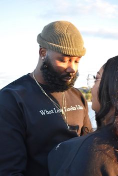 a man with a beard standing next to a woman wearing a sweater and beanie