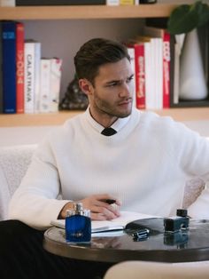 a man in a white sweater and tie sitting at a table with a book on it