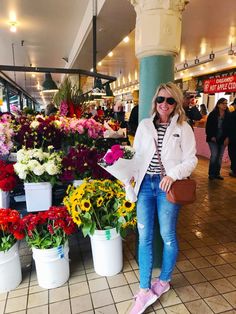 a woman standing in front of flowers at a market