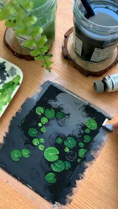 someone is painting some green leaves on a piece of black paper with watercolors