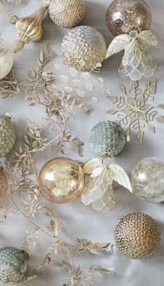 an assortment of glass ornaments on a white tablecloth with gold foil leaves and snowflakes