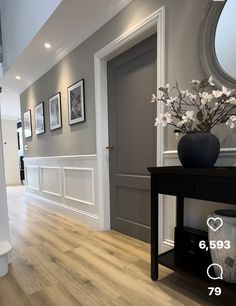 a vase with flowers is sitting on a table in front of a door and some framed pictures