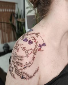 a woman's shoulder with flowers and vines tattooed on her left arm, in front of a couch