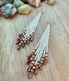 two pairs of white and brown beaded earrings on top of a wooden table next to rocks