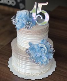 a white cake with blue flowers and the number fifteen on top is sitting on a table