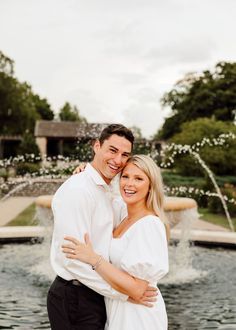 a man and woman hugging in front of a fountain