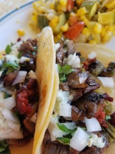 two tacos are sitting on a plate with corn and other foods in the background