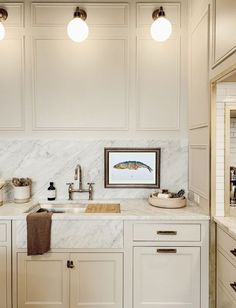 a kitchen with white cabinets and marble counter tops, two lights above the sink are hanging on the wall