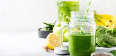 a green smoothie in a mason jar surrounded by other fruits and veggies