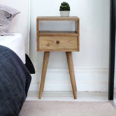 a small wooden table with a potted plant on it next to a bed in a bedroom