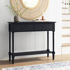 a console table with two drawers in front of a staircase and a round mirror above it