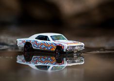 a toy car is sitting on the ground with its reflection in the water's surface