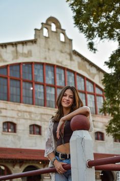 a beautiful young woman standing on top of a white fence next to a tall building