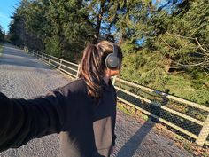 a woman riding a skateboard down a gravel road next to a fence and trees