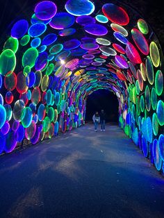 people are walking through an illuminated tunnel with colorful lights on the walls and in the ceiling