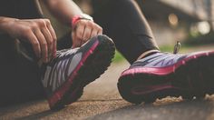 a person tying their running shoes while sitting on the ground