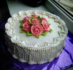 a white cake with pink roses on top sitting in front of a window sill