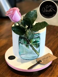 a pink rose sitting in a mason jar on top of a wooden table next to a price tag