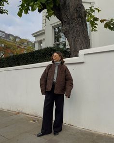 a woman leaning against a white wall on the sidewalk while talking on her cell phone