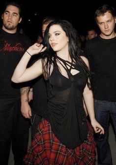 a woman in a black top and red plaid skirt standing next to two men wearing black t - shirts