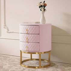 a pink and gold cabinet with flowers on top in a white room next to a wall