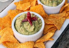 two small white bowls filled with guacamole and chips on a platter