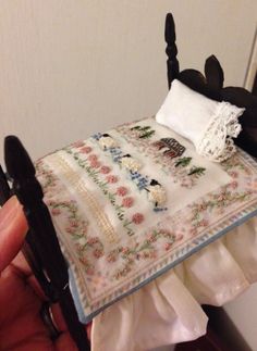 someone is holding a miniature doll with a quilt on it's bed and pillow