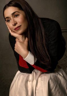 a woman with long hair wearing a black jacket and white dress posing for the camera