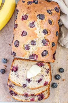 a loaf of blueberry bread sitting on top of a wooden cutting board next to bananas