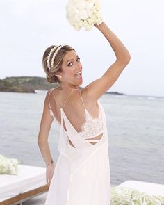 a woman in a white dress holding a bouquet of flowers on her head and looking at the camera