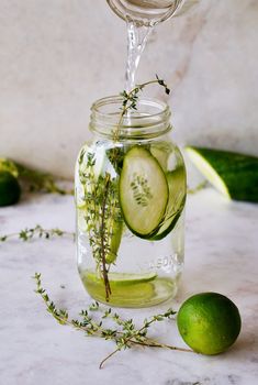 cucumber slices and herbs in a mason jar with water being poured into it