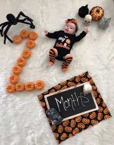 a baby laying on top of a white blanket next to halloween decorations and a sign