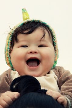 a smiling baby wearing a knitted hat with a horn on it's head