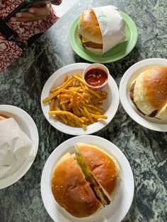 plates with hamburgers and fries on them sitting on a marble counter top next to a cell phone