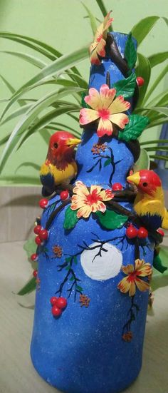 a blue vase with birds and flowers painted on it's sides, sitting next to a potted plant