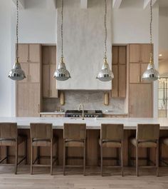 a large kitchen with wooden cabinets and white marble counter tops, hanging lights over the island