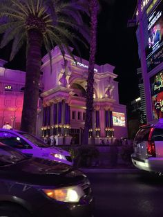 cars are parked in front of a building at night with palm trees and neon lights