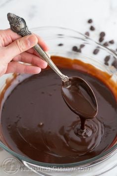 a person is spooning chocolate into a glass bowl filled with melted chocolate and coffee beans