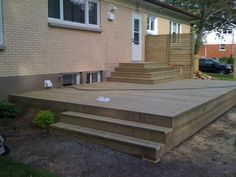 a wooden deck in front of a house with steps leading up to the side door