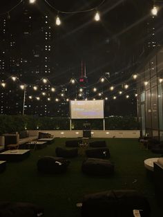 an outdoor movie theater is lit up at night with lights strung from the ceiling and bean bags on the ground