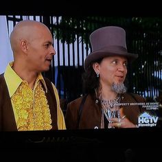 two men in hats are talking to each other on the television screen, one is wearing a yellow shirt and the other wears a brown jacket