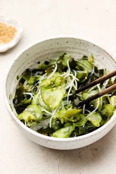 a white bowl filled with green vegetables and sprouts next to two chopsticks