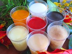 several cups filled with different colored liquids on top of a wooden table next to flowers