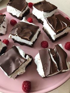 several pieces of chocolate dessert on a pink plate with raspberries and cream frosting